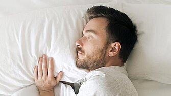 Schlafender Mann in weißem Bett auf der Obersicht. Entspannt, bärtig, bärtig, in einem gemütlichen weißen Schlafzimmer