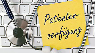 Das Wort "Patientenverfügung" steht auf einem Post-It Zettel, der auf einer Tastatur liegt.