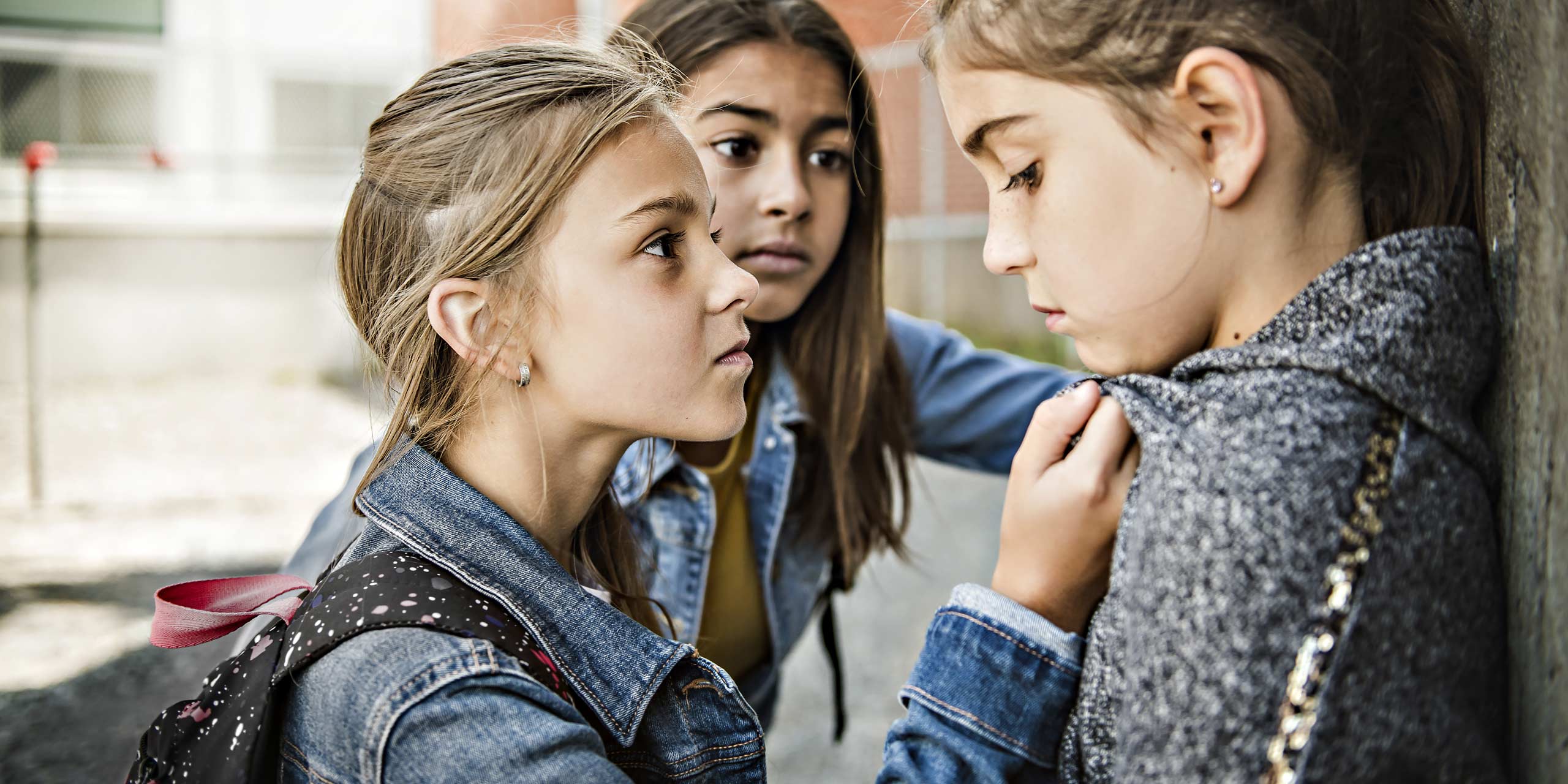 Zwei junge Mädchen drangsalieren ein drittes Mädchen, welches am Kragen festgehalten wird.